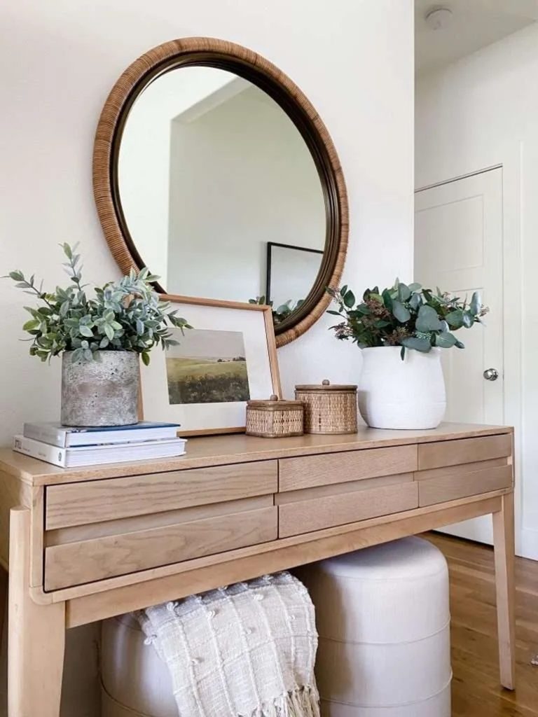 a brown console table with flowers planters and a mirror above it 