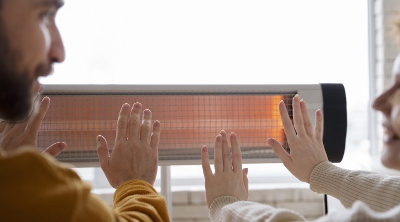 man and woman heating their hands on electric heater